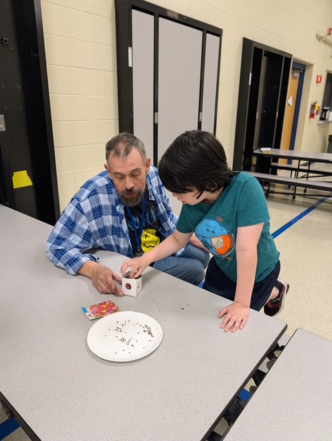 Un miembro del personal y un alumno plantan semillas juntos en una pequeña maceta hecha a mano durante una actividad con motivo del Día de la Tierra en el Northwest Center for Autism.