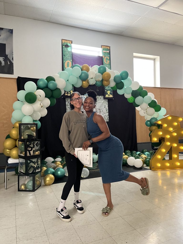 Phoenix Academy senior smiling with staff member while holding a graduation certificate during the Class of 2026 luncheon celebration
