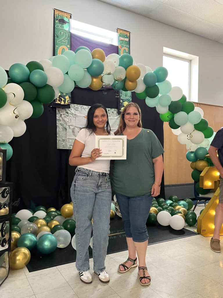 Phoenix Academy graduate smiling beside staff member while holding certificate of graduation during senior recognition event