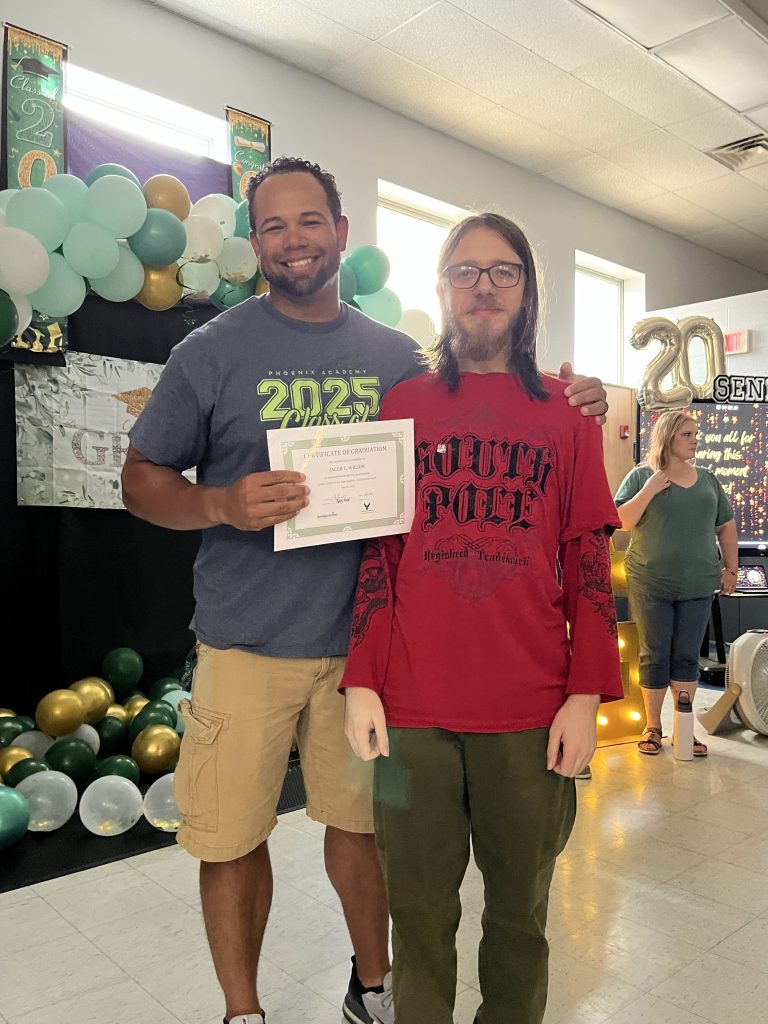 Phoenix Academy senior posing with staff member and graduation certificate during the Class of 2026 celebration luncheon