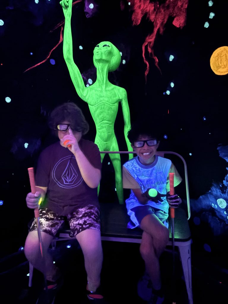 Two Sierra students smiling while playing glow-in-the-dark mini golf during a Fun Friday outing in Gilbert.