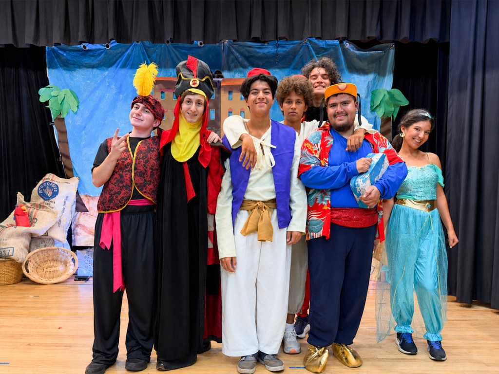 Students dressed in Aladdin costumes perform together on stage during the Sierra School of San Diego theater production.