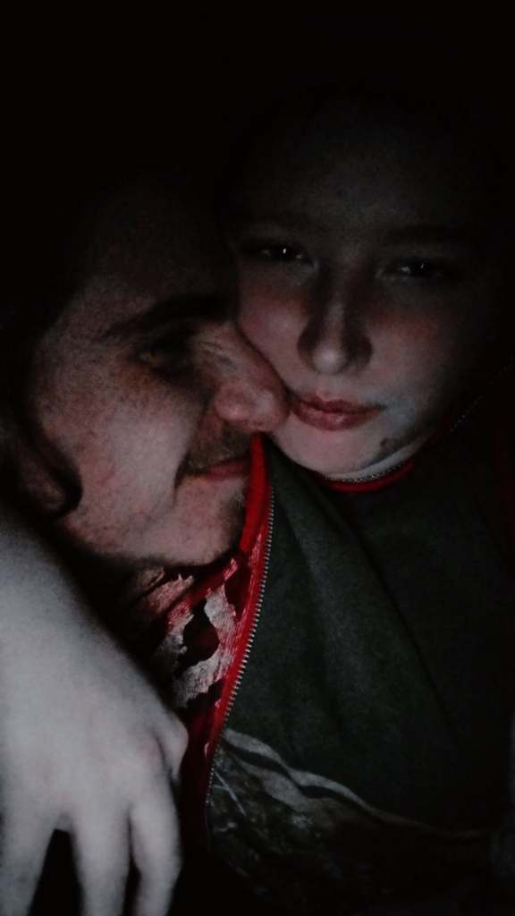 Two individuals share a close embrace in a dimly lit setting.