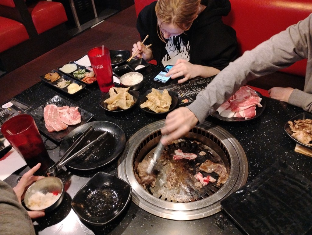 people enjoy cooking meat at a restaurant table while dining with chopsticks.