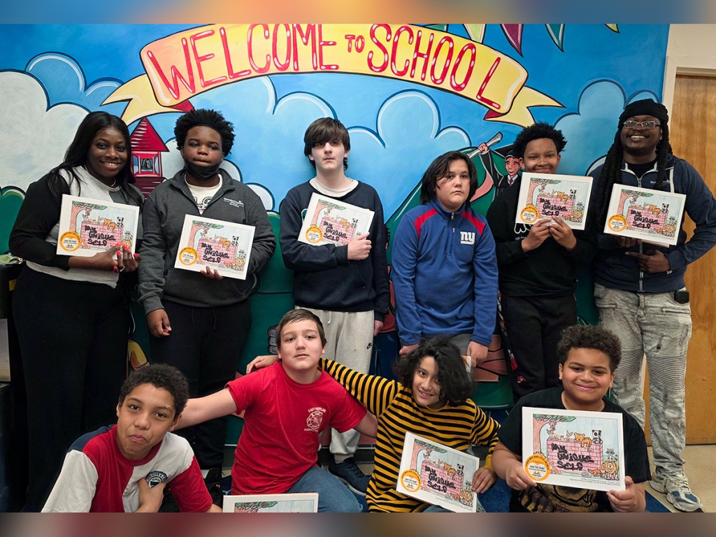 Students proudly holding copies of their My Unique Self books in front of a welcome wall at High Road School of Wallingford.