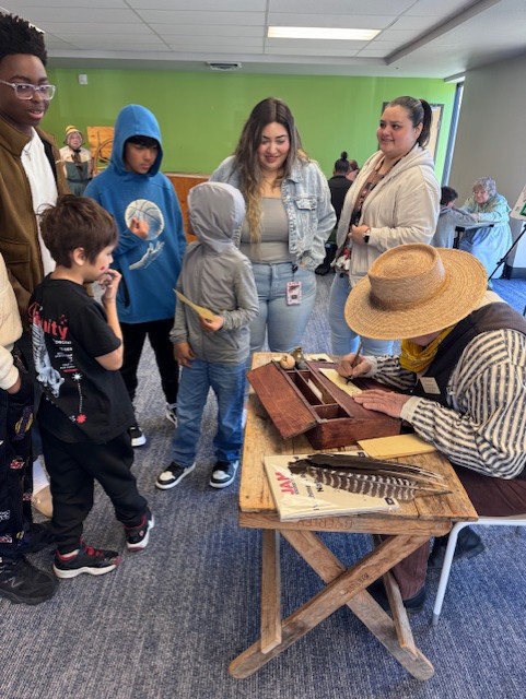 Exhibitor in historical clothing showing students old-fashioned writing materials
