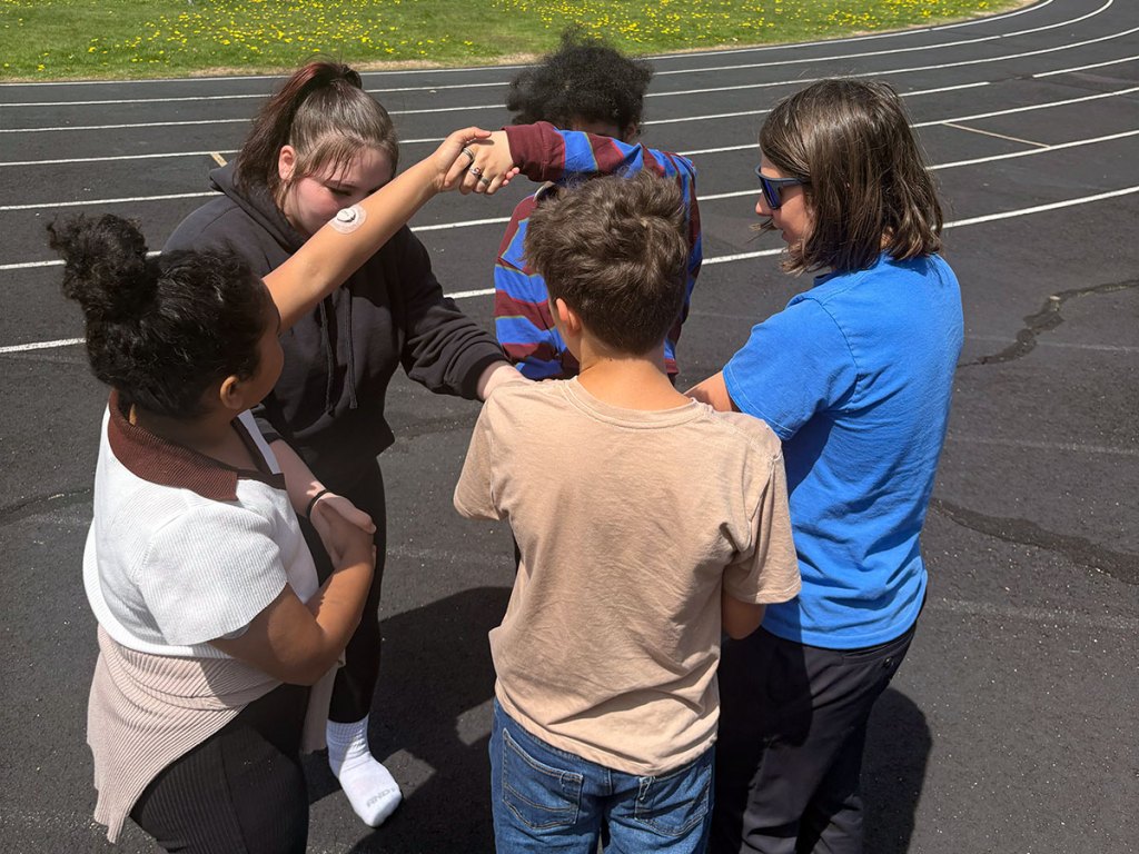 Students and staff participate in a group activity outdoors near a racetrack during Autism Acceptance Month activities at Camino Alto IDC.