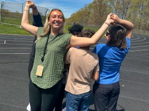 Staff member smiles while holding hands with students during an outdoor group activity near the school track.