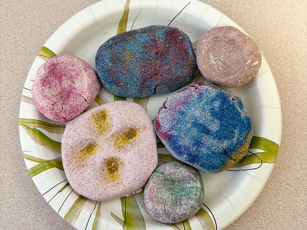 Decorated worry stones with glitter and colorful paint displayed on a table after a classroom mindfulness activity.