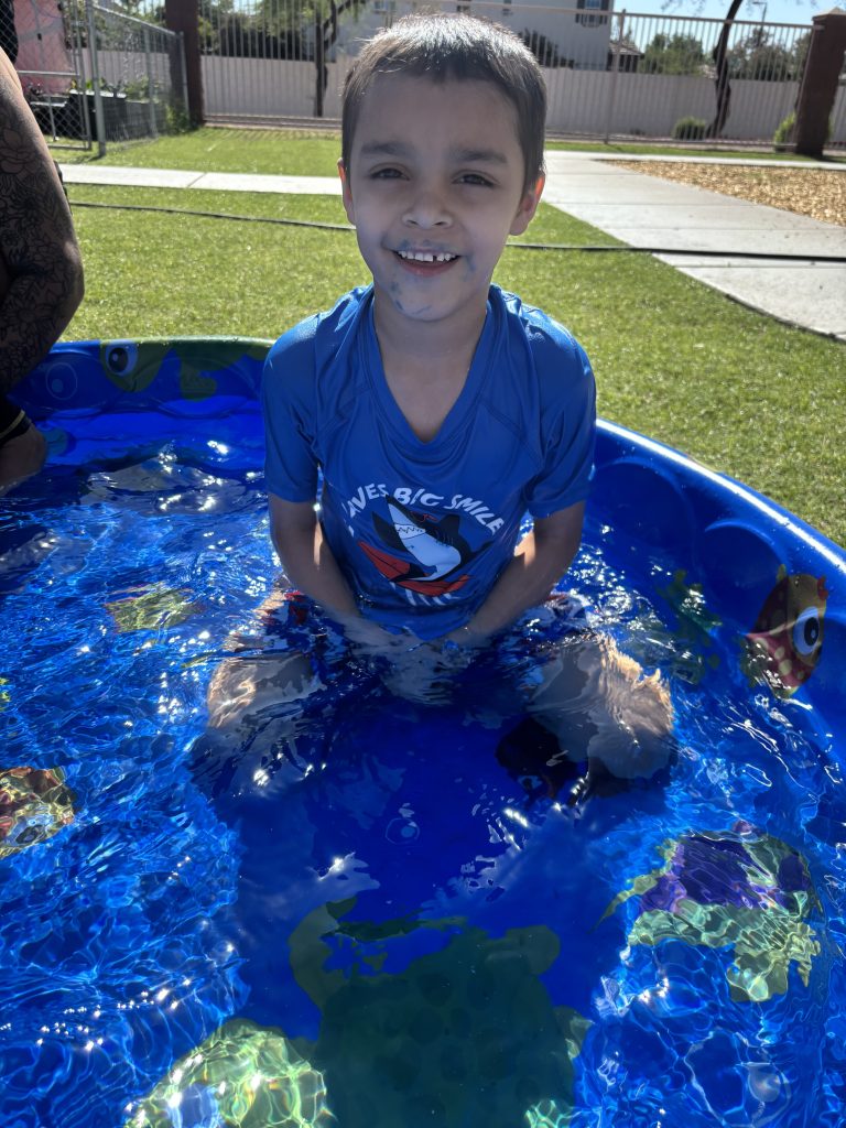 Una niña sonríe sentada en una pequeña piscina infantil azul durante la fiesta «Summer Splash Bash» de Sierra Gilbert.