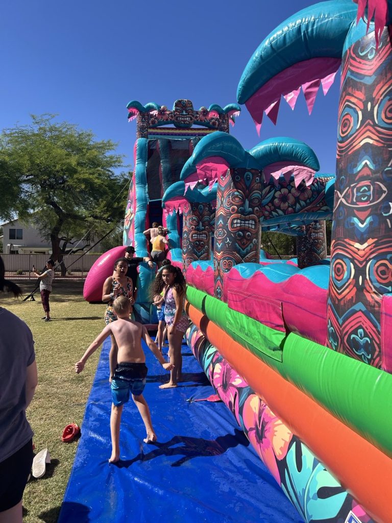 Los alumnos y sus familias se reunieron alrededor del tobogán acuático hinchable durante la fiesta «Summer Splash Bash» de Sierra Gilbert.