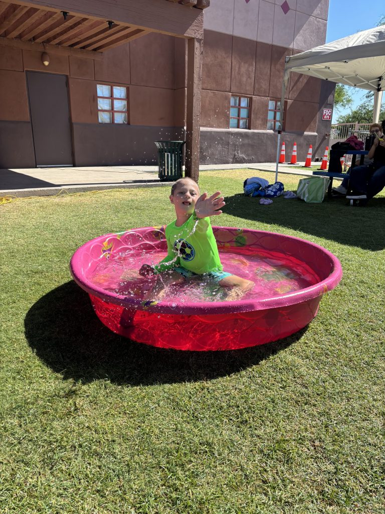 Un alumno chapotea en una piscina infantil rosa durante las actividades de verano al aire libre en Sierra Gilbert.