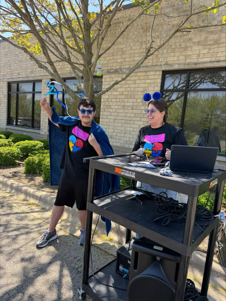 Staff member and student smiling during a school celebration while wearing matching shirts, colorful accessories, and festive decorations.