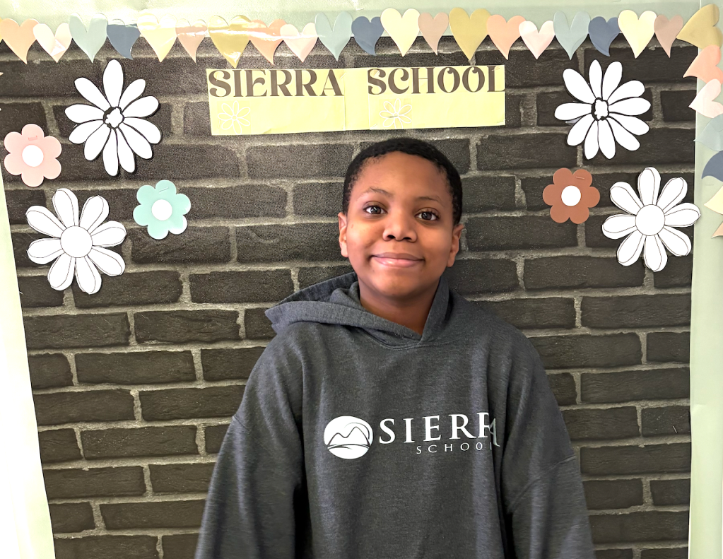 Student Josiah posing in front of a Sierra School display board decorated with flowers and hearts at Sierra School at McKinney