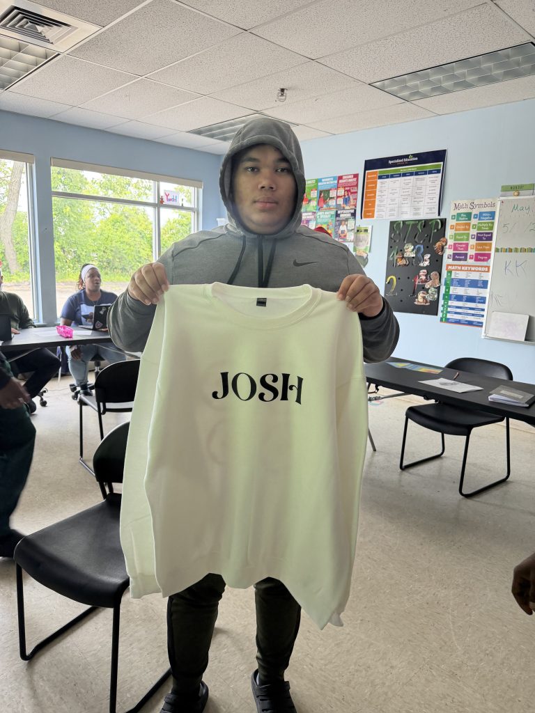 Un estudiante muestra una sudadera personalizada con su nombre impreso en la parte delantera tras completar el proceso de diseño y confección.
