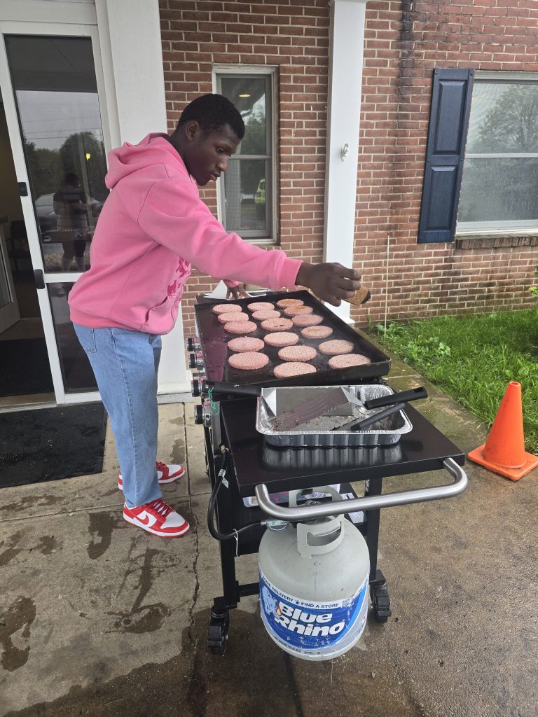 Un alumno prepara hamburguesas en una plancha durante la barbacoa anual del colegio.