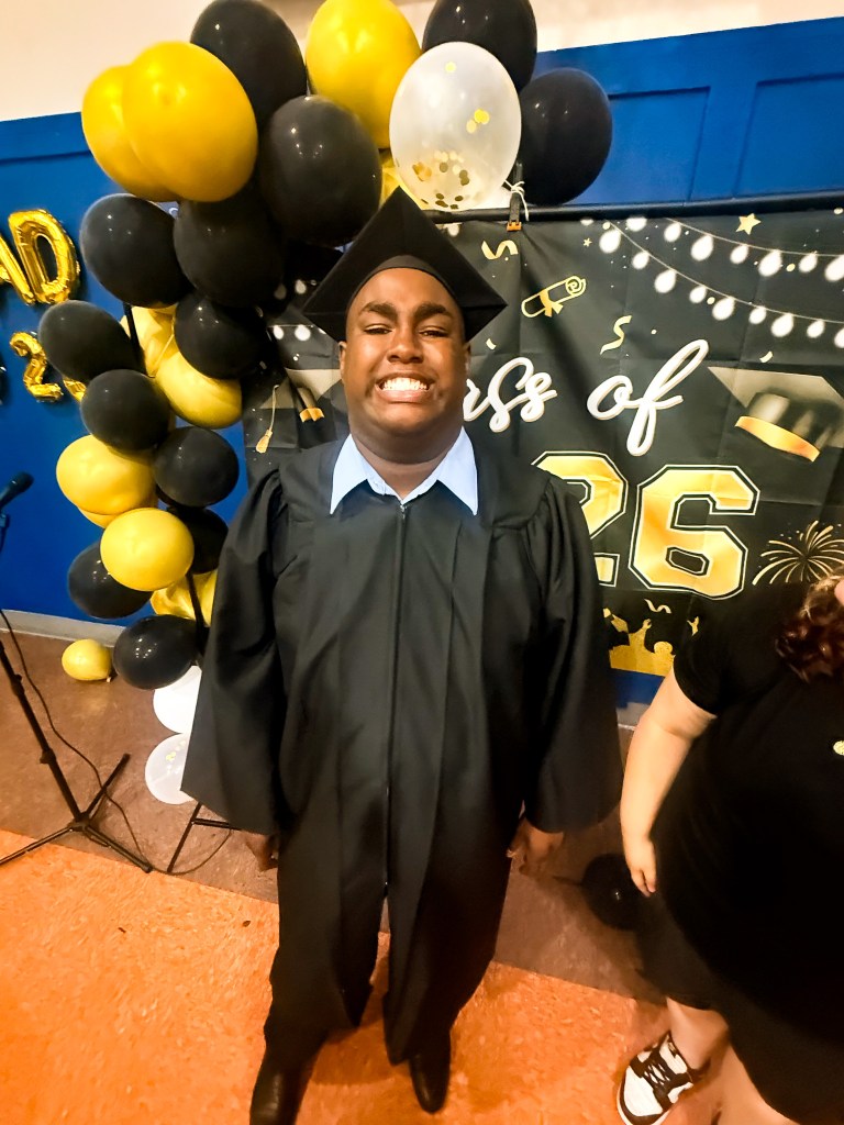 Una graduada de la High Road School de Hartford sonríe con toga y birrete junto a los adornos en negro y dorado de la promoción de 2026.