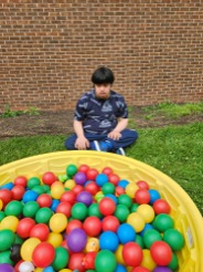 Matthew participating in an outdoor activity beside a pool of colorful balls.