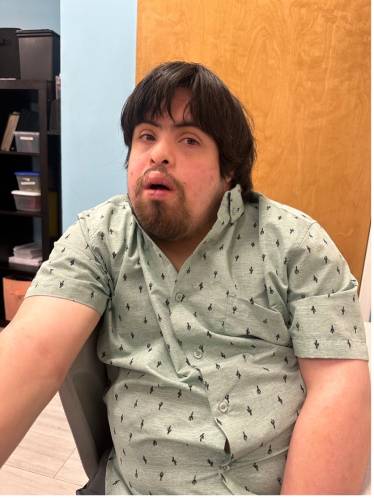 Matthew seated at a table in a patterned green shirt at BEST Academy.