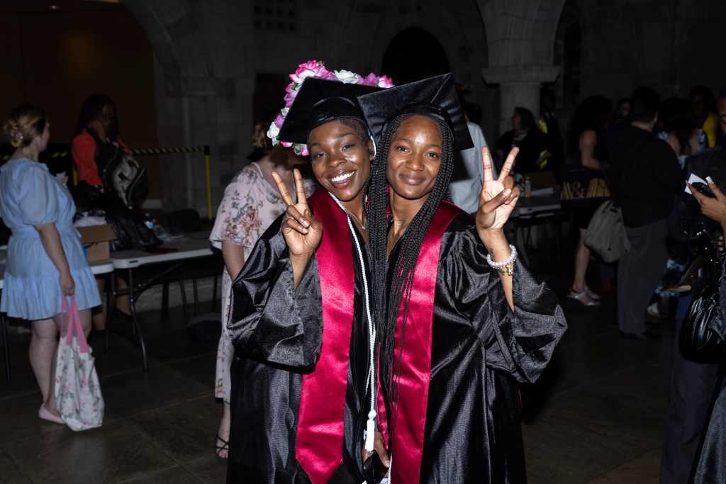 Two Class of 2026 graduates smile and hold up peace signs after graduation.