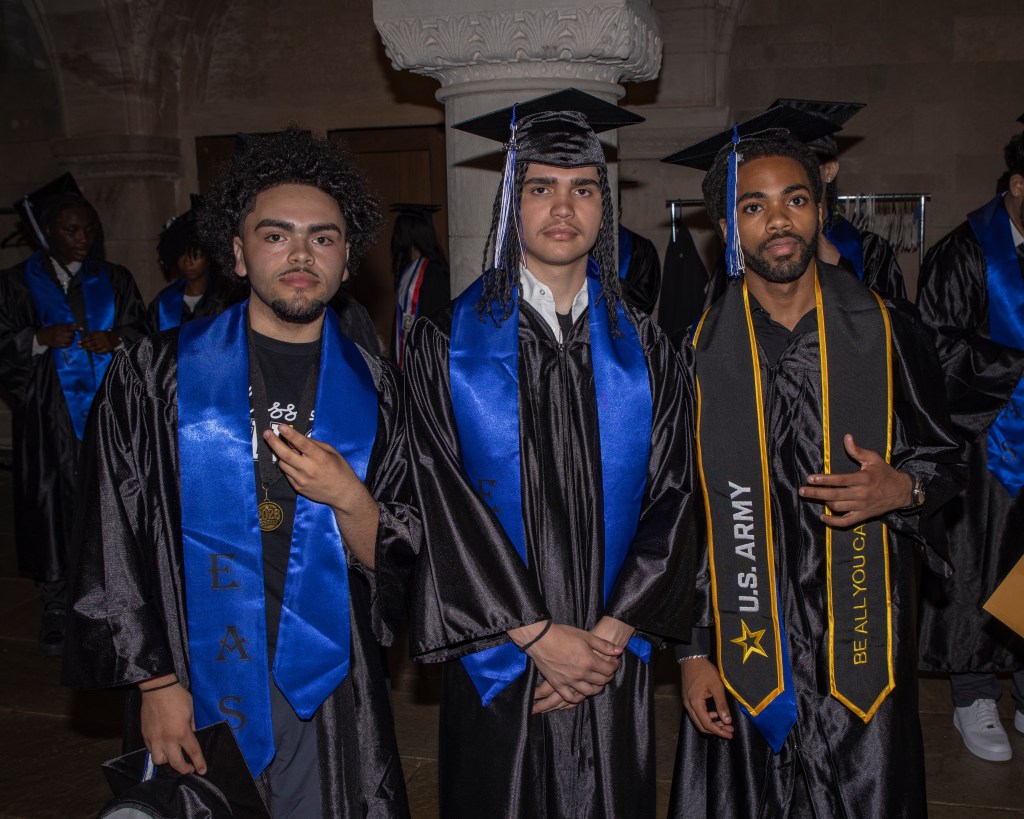 Three graduates wearing blue and military-themed stoles pose together before the ceremony.