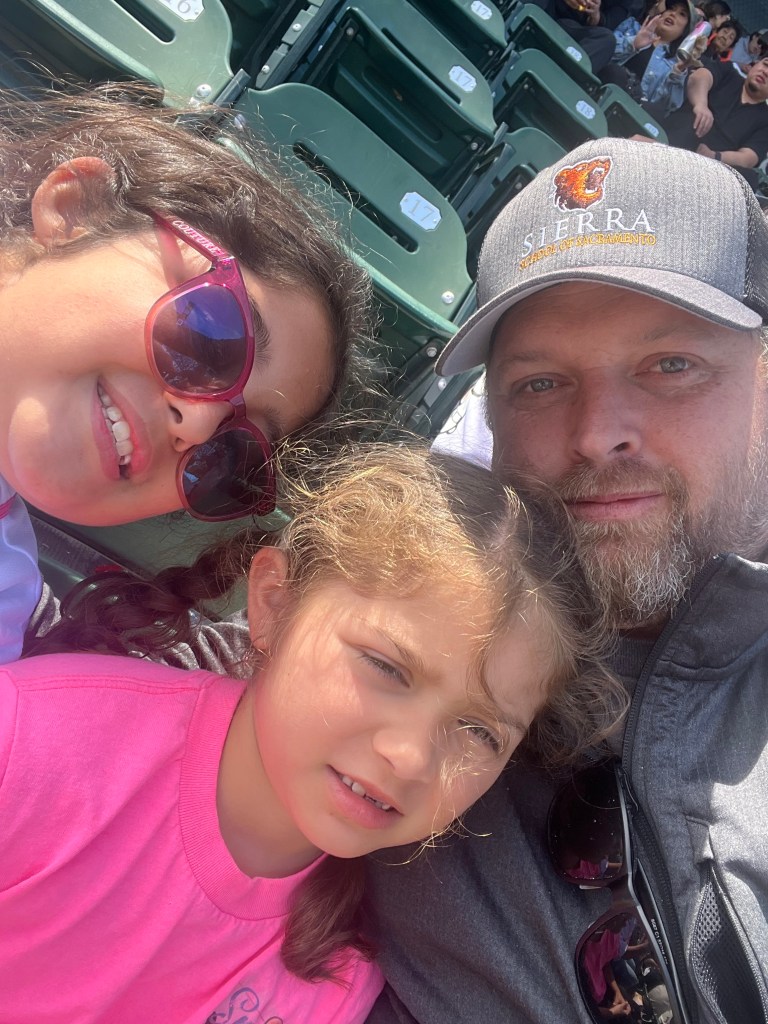 Dustin Hefner poses with his two daughters at a baseball game.