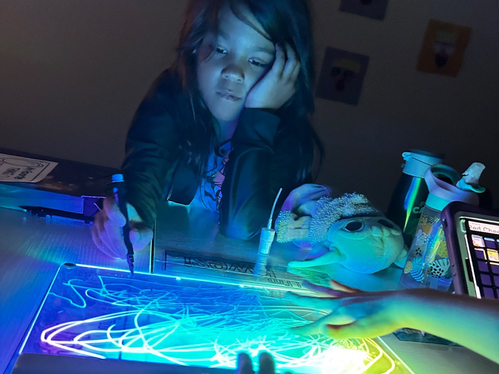 Un alumno crea diseños coloridos en una mesa de dibujo iluminada durante una actividad de clase del programa ESY en la High Road School de Wright City.
