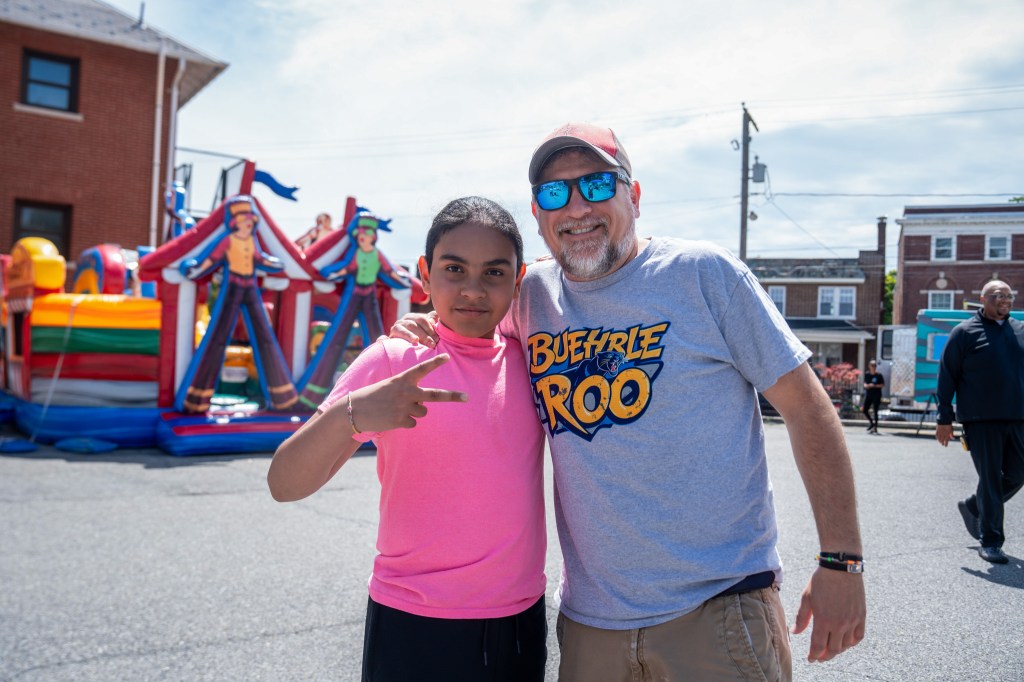 Un alumno y un miembro del personal posan juntos delante de las atracciones hinchables durante la fiesta de fin de curso de Buehrle-Roo en la Academia Buehrle.
