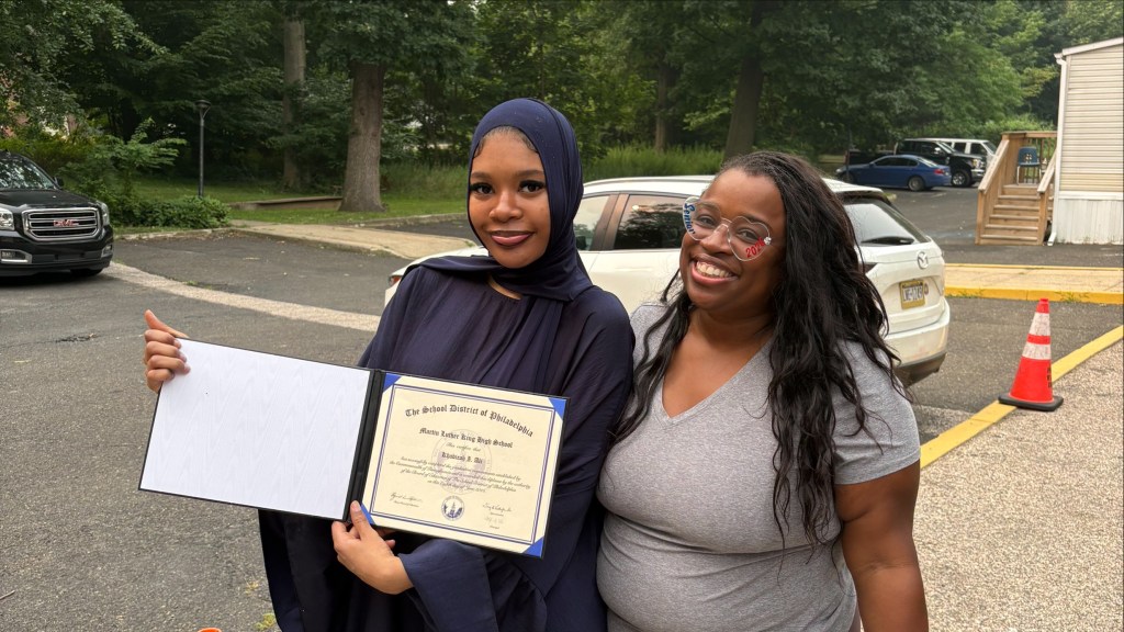 Una graduada muestra su título mientras posa junto a un miembro del personal en la ceremonia de graduación de la escuela de verano de Filadelfia.
