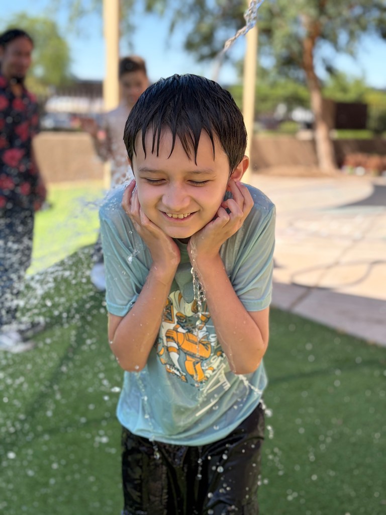 Student smiles under an outdoor water spray during a Sierra Schools of Arizona ESY summer learning celebration.