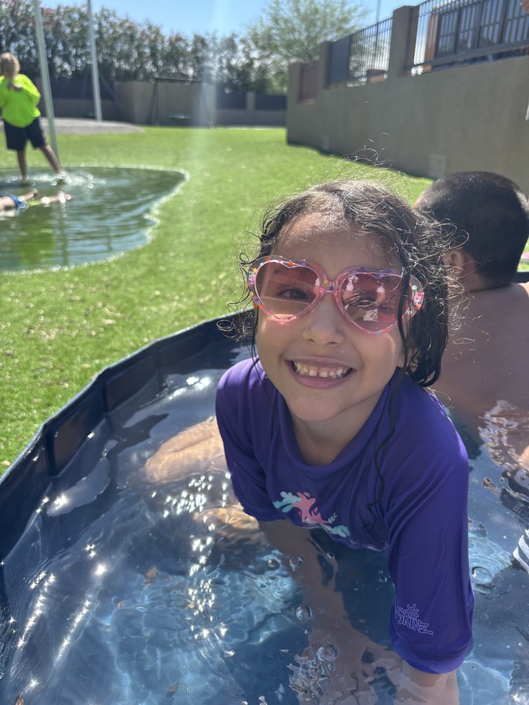 Student smiles in an outdoor pool during a Sierra Schools of Arizona ESY summer celebration.