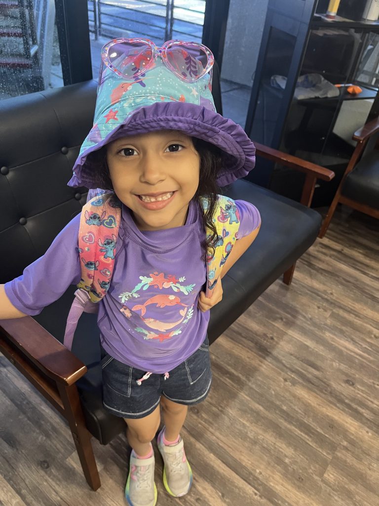 Student smiles while wearing a backpack, sun hat and sunglasses during summer activities at Sierra Schools of Arizona.