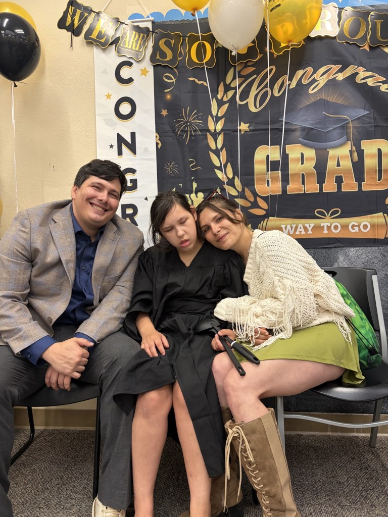 Lattice graduate wearing a black cap and gown standing with a staff member inside a classroom.