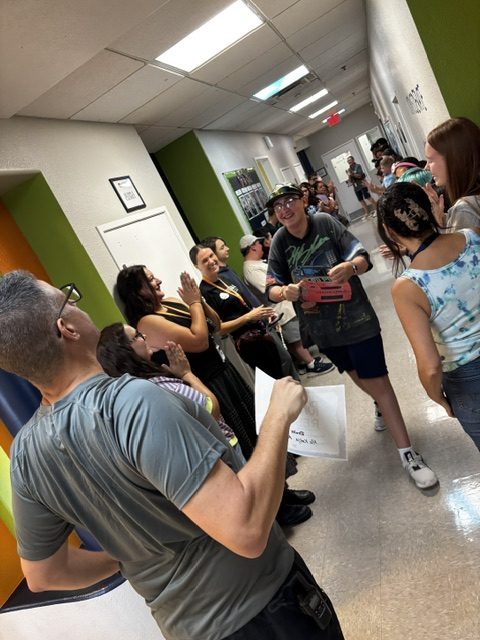 A smiling Sierra Gilbert student receives recognition while staff and classmates applaud in the hallway.