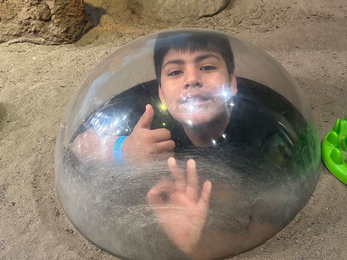 High Road School student smiles and gives a thumbs up while looking through an aquarium viewing bubble.