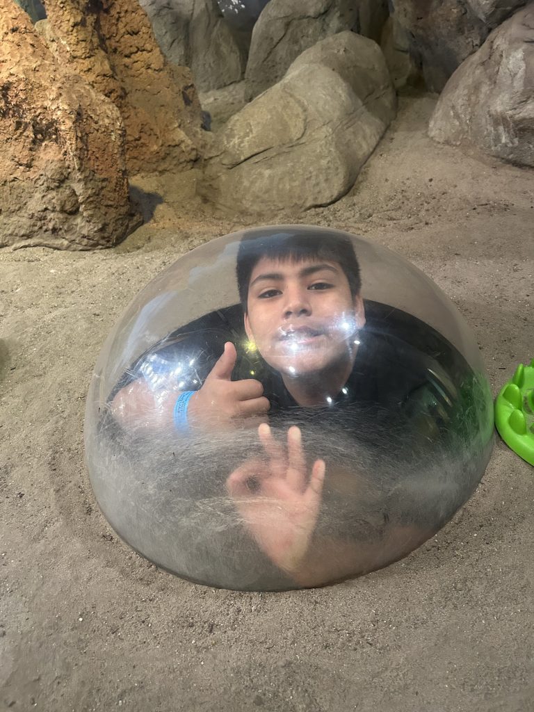 High Road School student smiles and gives a thumbs up while looking through an aquarium viewing bubble.