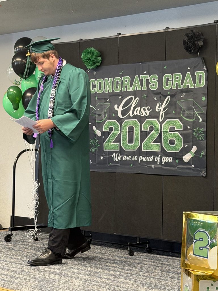 Un graduado de la Sierra School del condado de Solano posa junto a un expositor de la promoción de 2026.