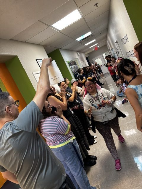 A Sierra Gilbert student smiles while walking through a hallway of cheering staff and classmates during a respect celebration.