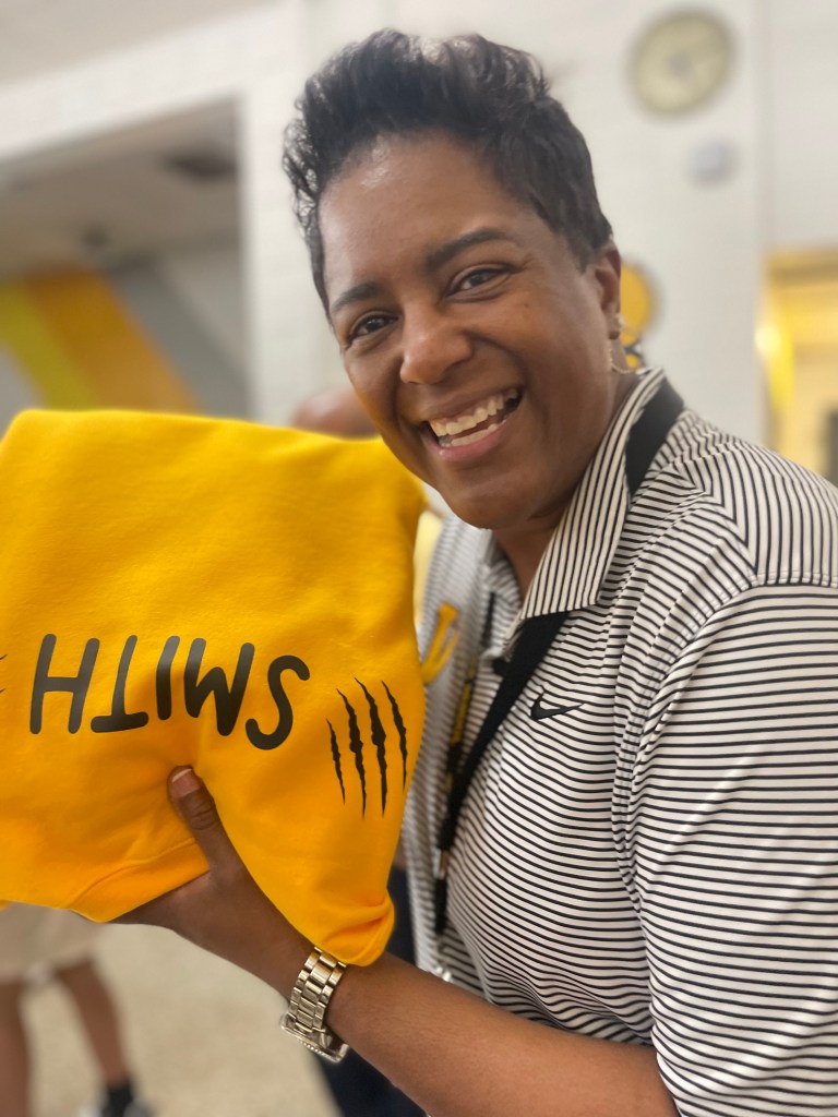 Sabrina Smith sonríe mientras sostiene su jersey dorado personalizado durante el acto de reconocimiento del colegio.