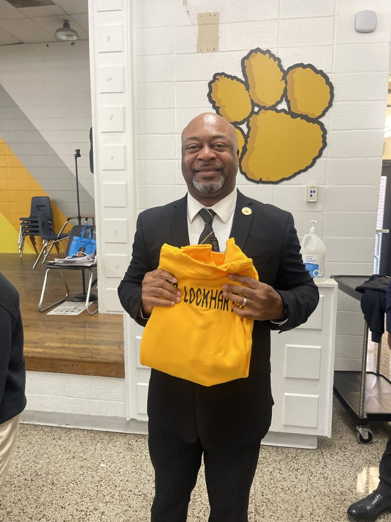 El Dr. Craig Lockhart sostiene su jersey dorado personalizado durante un acto de homenaje celebrado en la Escuela de Estudiantes Destacados de la ciudad de Valdosta.