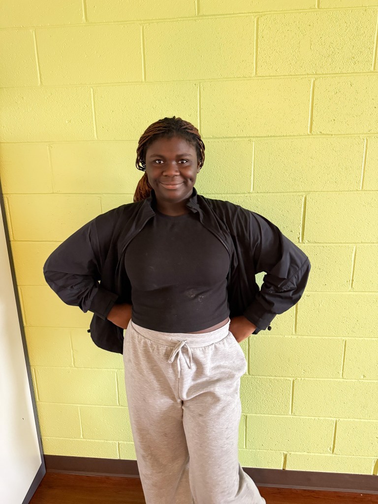 Aniyah, a student at High Road School of Bucks County, smiling with her hands on her hips against a yellow wall.