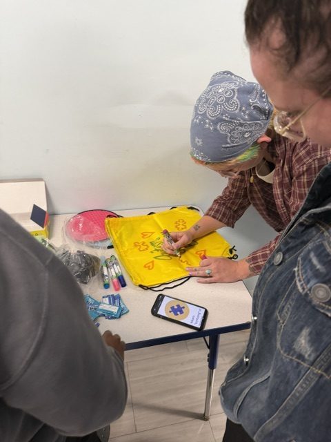 B.E.S.T. Academy staff decorating a yellow sensory bag with markers and autism awareness designs.
