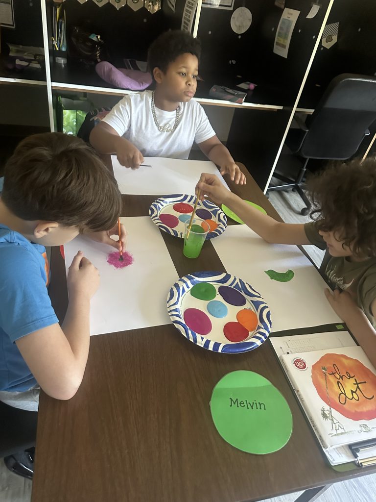Students paint colorful dot artwork together during a classroom art and literacy activity.