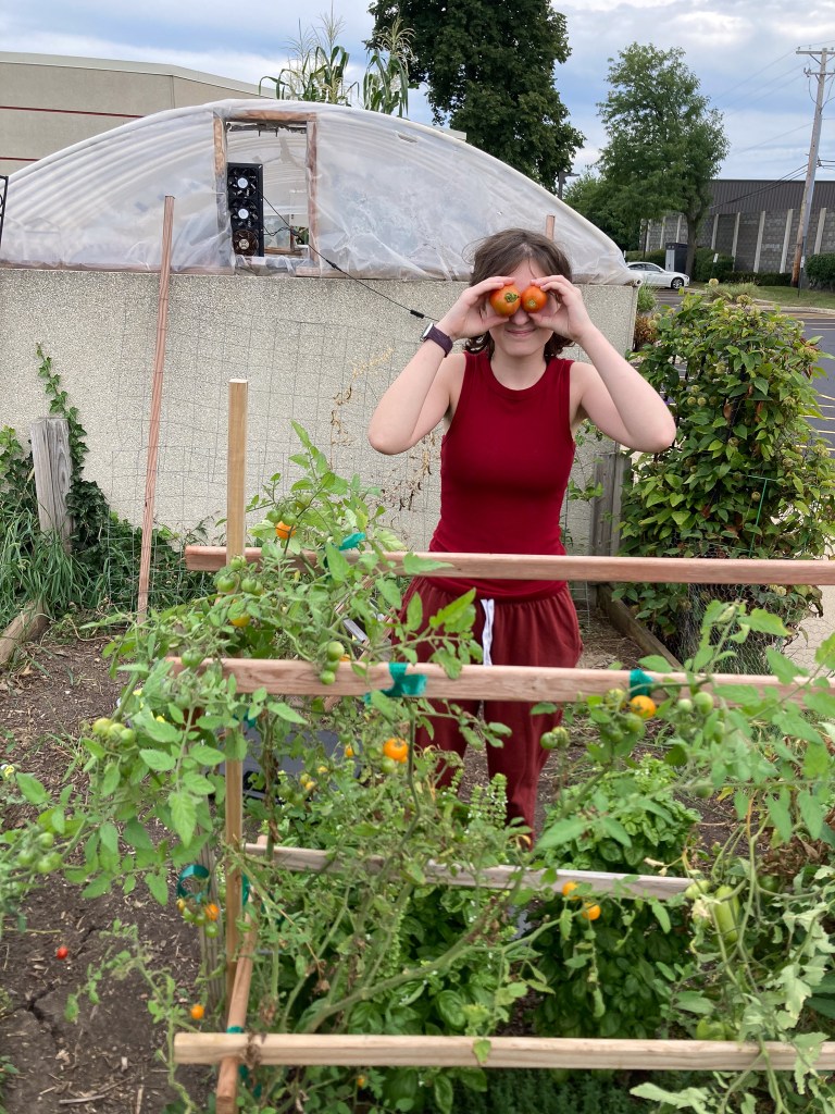 Un alumno de la NewHope Academy posando en el huerto con tomates recién cosechados