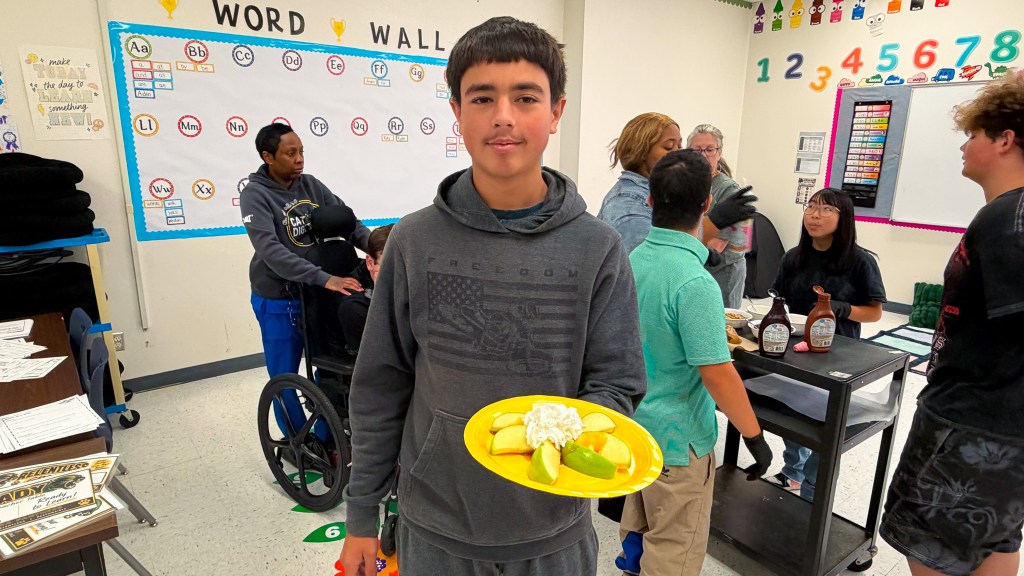 Student smiles while holding a plate of apples and toppings during the Sierra School at Krum apple bar activity.
