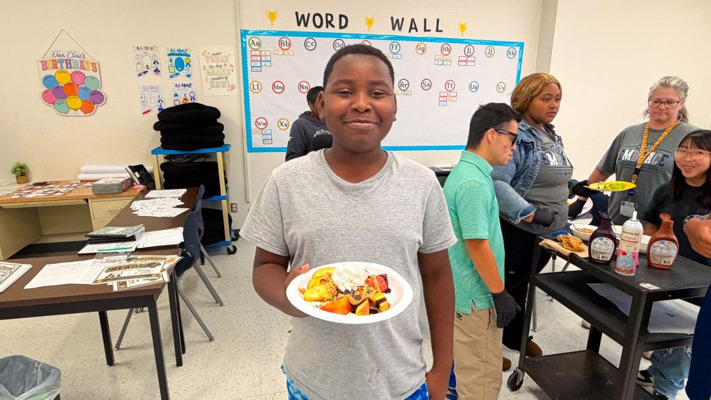 Student holds a plate of apples and whipped cream during a joint Sierra School at Krum and EMBRACE activity.