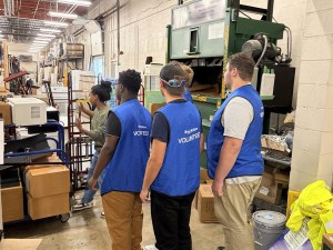 Los alumnos de la High Road School de Nashville, que llevan chalecos azules de voluntarios, posan junto a maquinaria industrial en la tienda ReStore de Hábitat para la Humanidad.