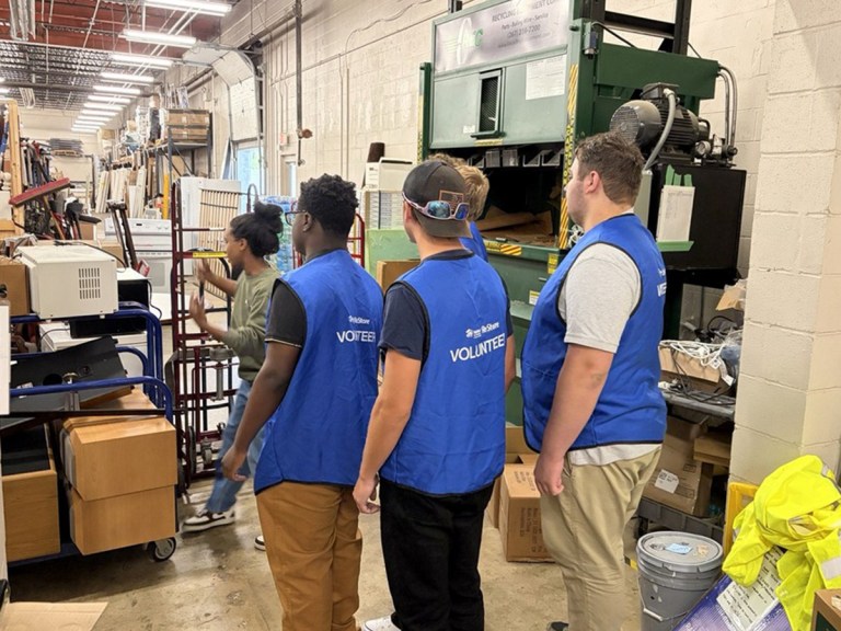 High Road School of Nashville students wearing blue volunteer vests stand near industrial equipment at Habitat for Humanity ReStore.