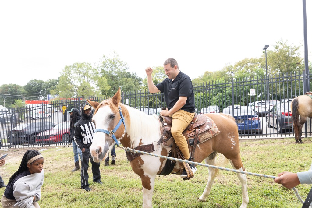 Un miembro del personal de Achieve Academy East sonríe mientras monta a caballo durante la visita de los Concrete Cowboys.