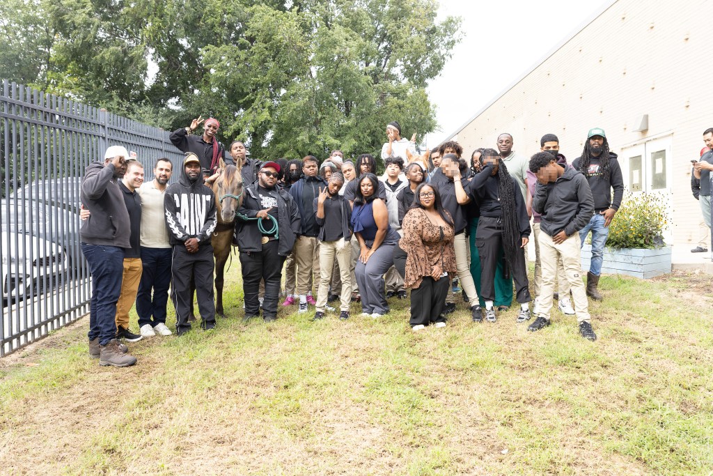 Los alumnos y el personal de Achieve Academy East posan para una foto de grupo con un caballo durante la visita a la escuela de Concrete Cowboys.